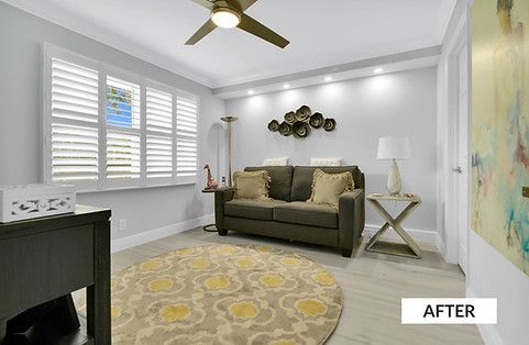 A renovated living room with a green couch, round rug, and window shutters.