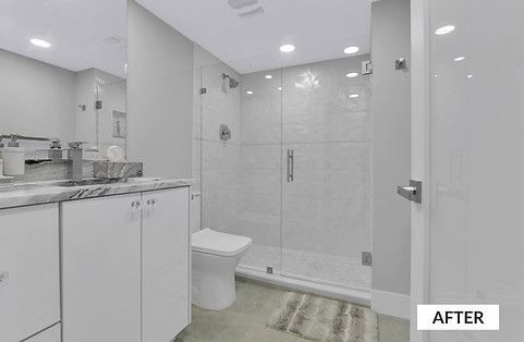 Modern white bathroom with glass shower, toilet, and vanity with marble countertop.