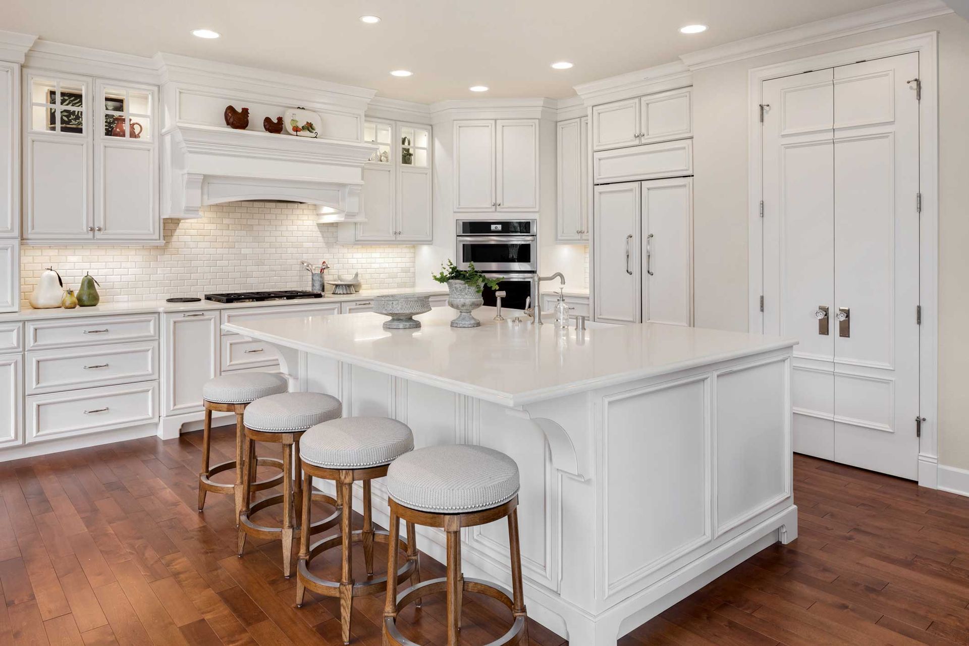 White kitchen with island, stools, wood floor, and stainless steel appliances.