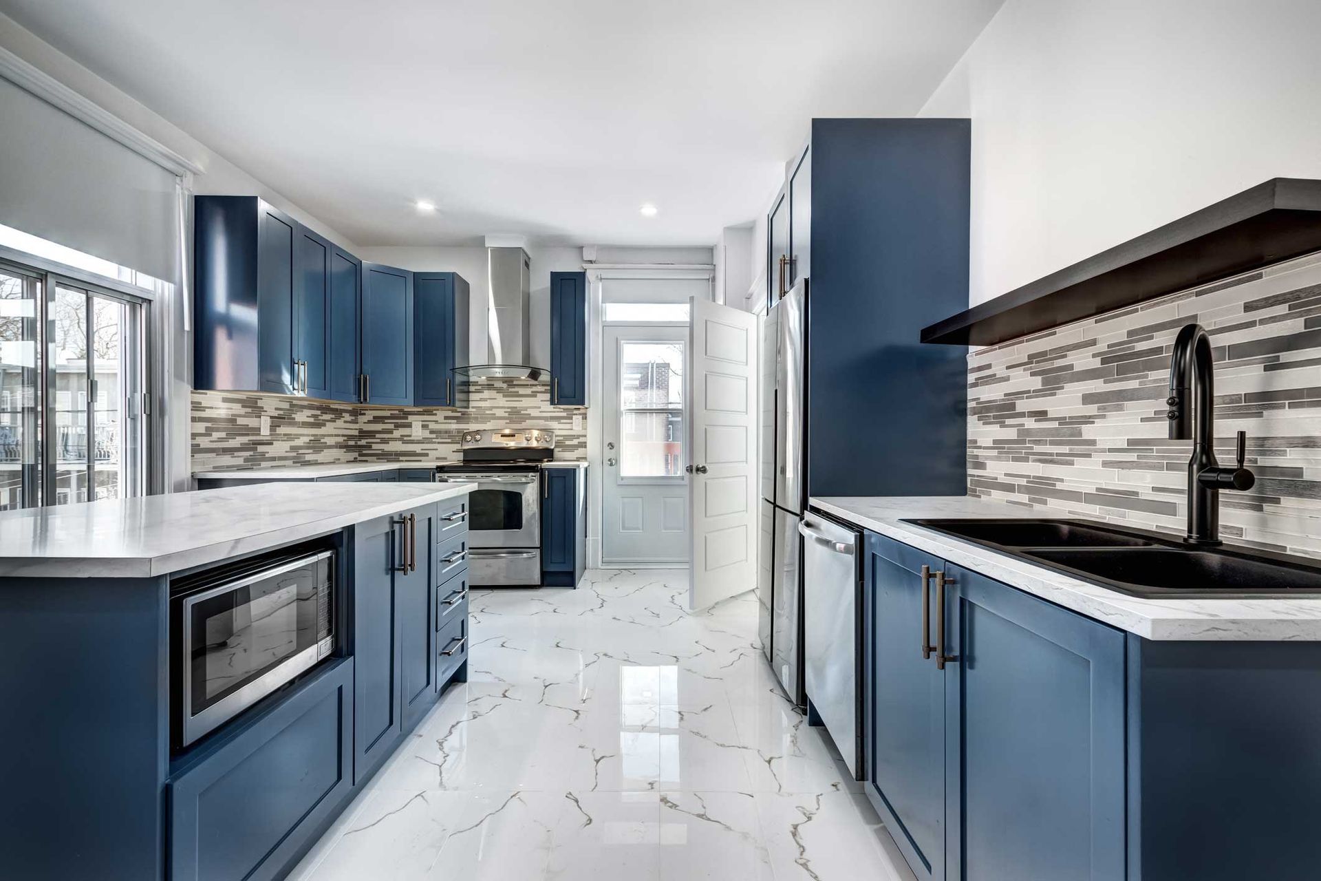 Modern kitchen with blue cabinets, white countertops, stainless steel appliances, and white tile floor.