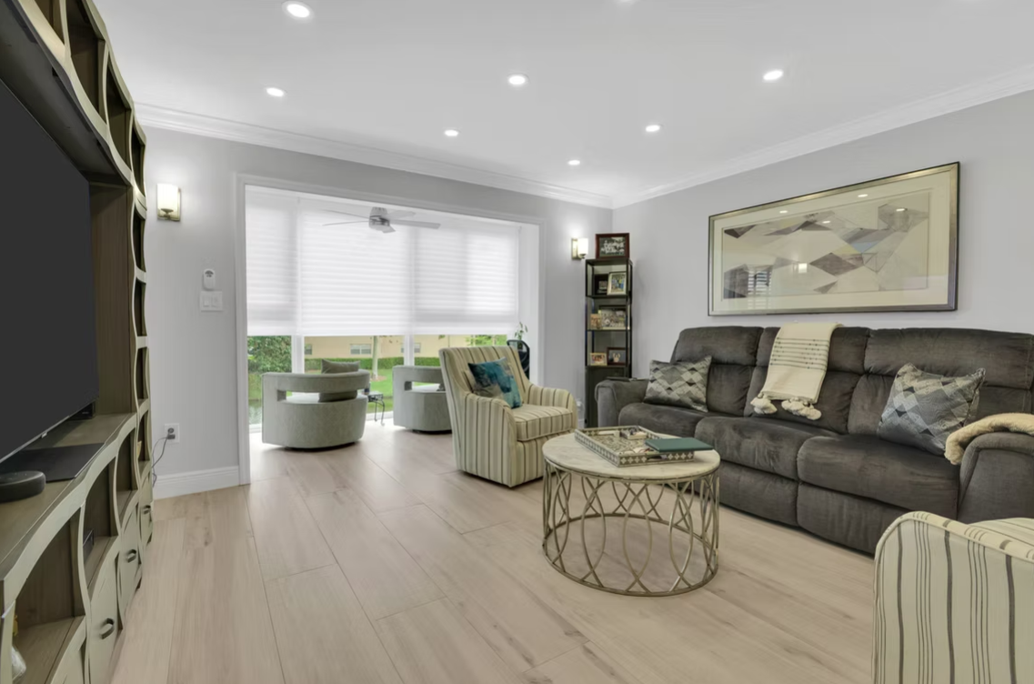 Living room with gray walls, light wood floor, gray sofa, armchairs, coffee table, and large window.