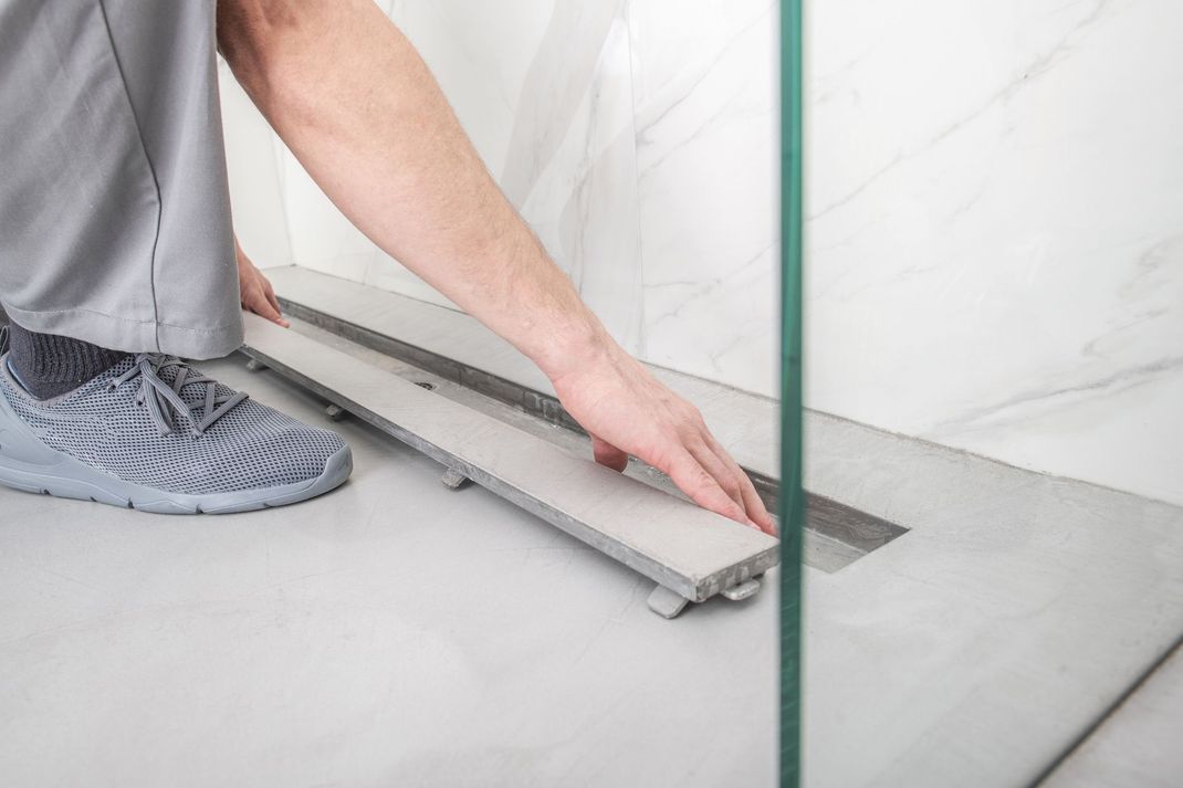 Contractor installing linear shower drain in modern bathroom tile renovation.