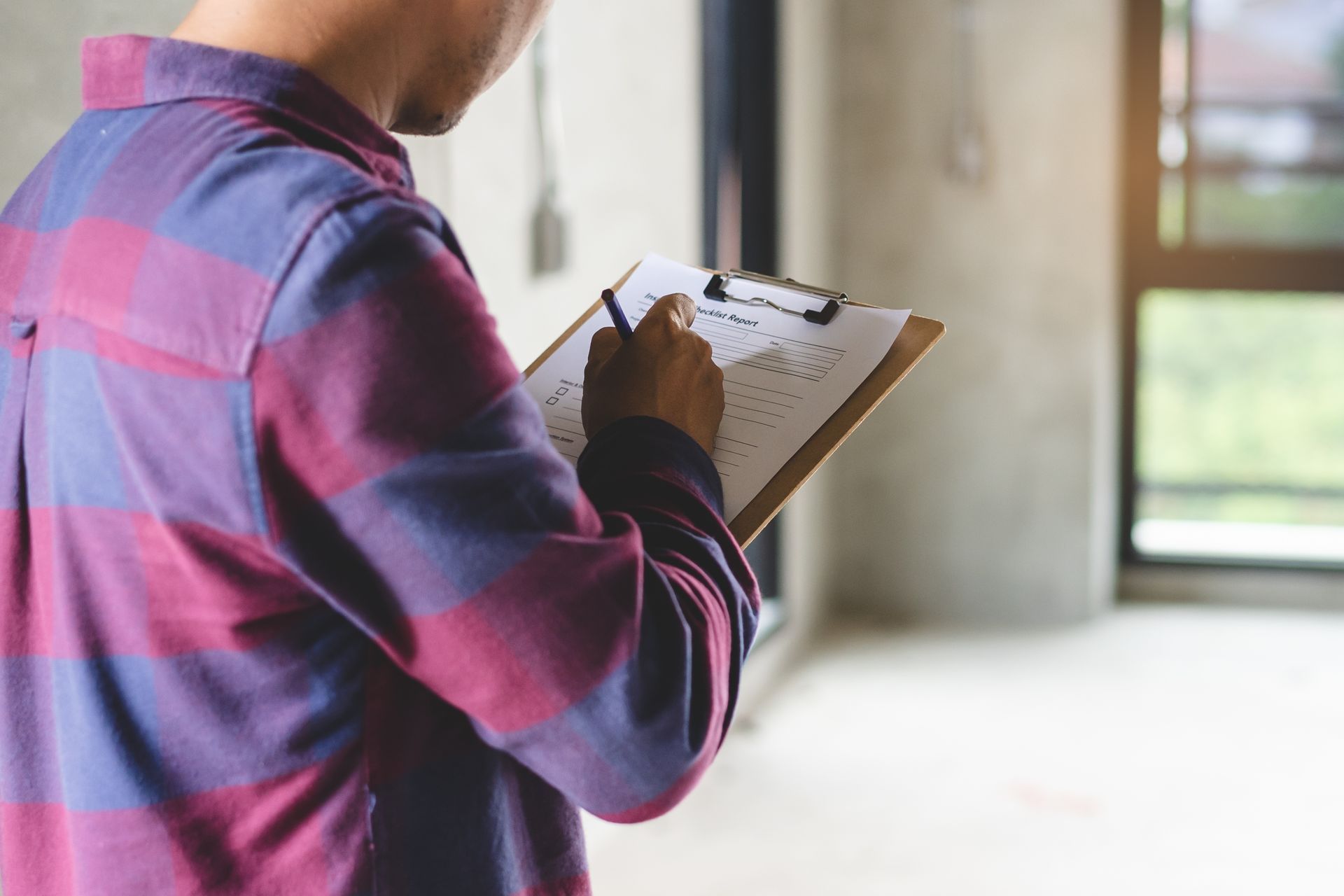 A man in a plaid shirt is holding a clipboard and writing on it.