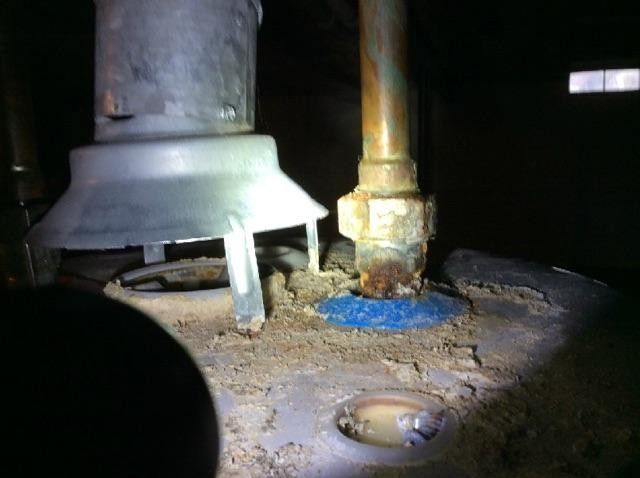A person is looking at a water heater with a flashlight.