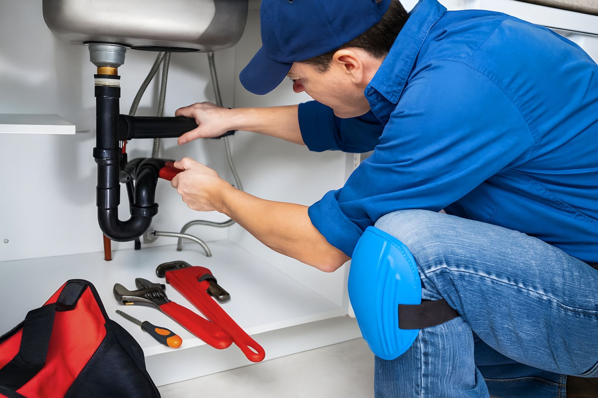 A plumber using a wrench to fix an under-sink drain for emergency plumbing contractors service.