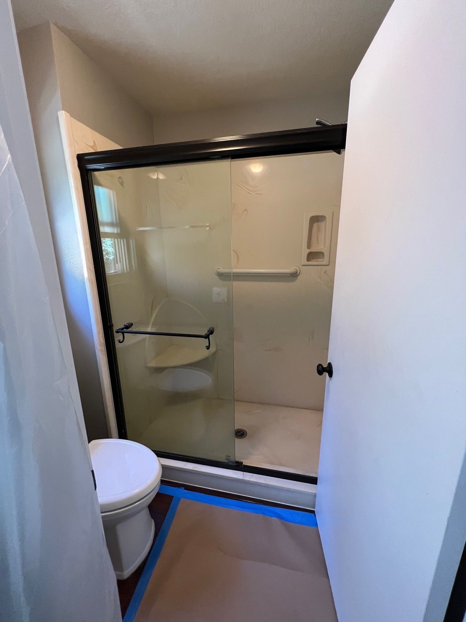 Bathroom with a shower, toilet, and a partially open white door. The shower has a black frame.