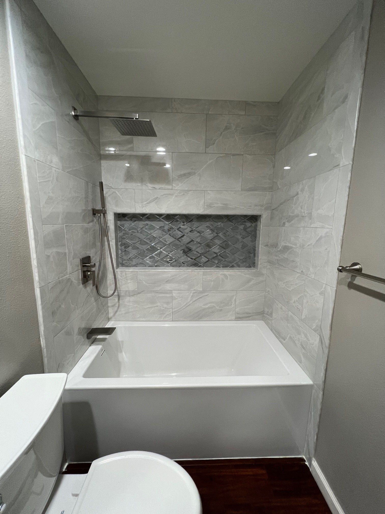 Modern bathroom with white tub, tiled walls, and toilet.