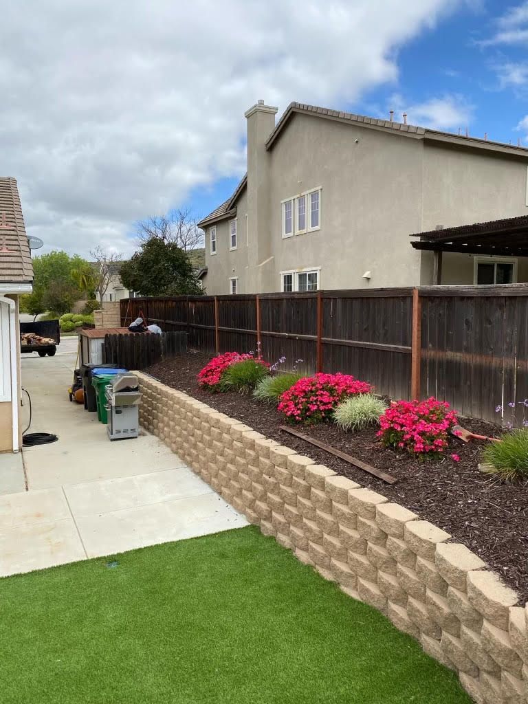 A backyard with a brick wall and flowers in front of a house.