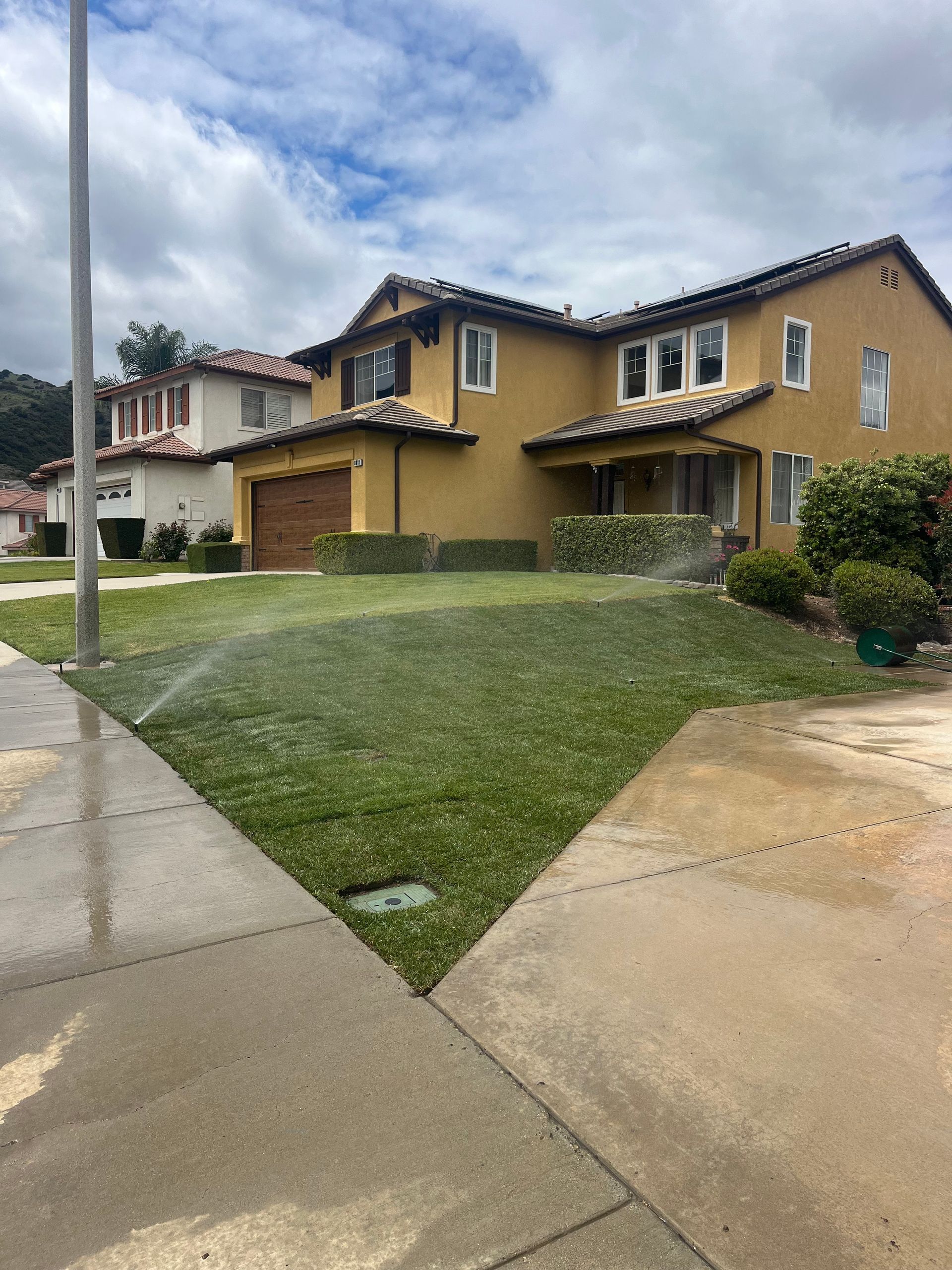 Suburban houses with tan stucco and a wet driveway and lawn under a cloudy sky