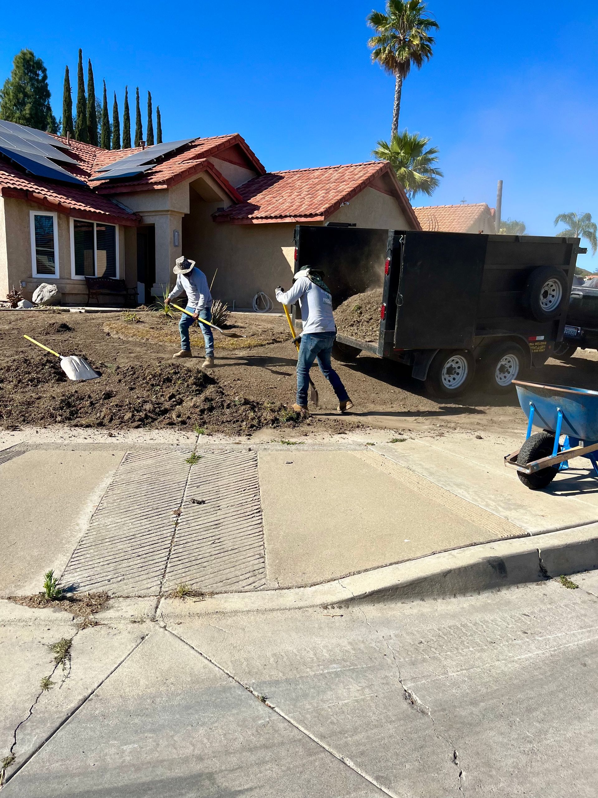 Two men are digging in the dirt in front of a house