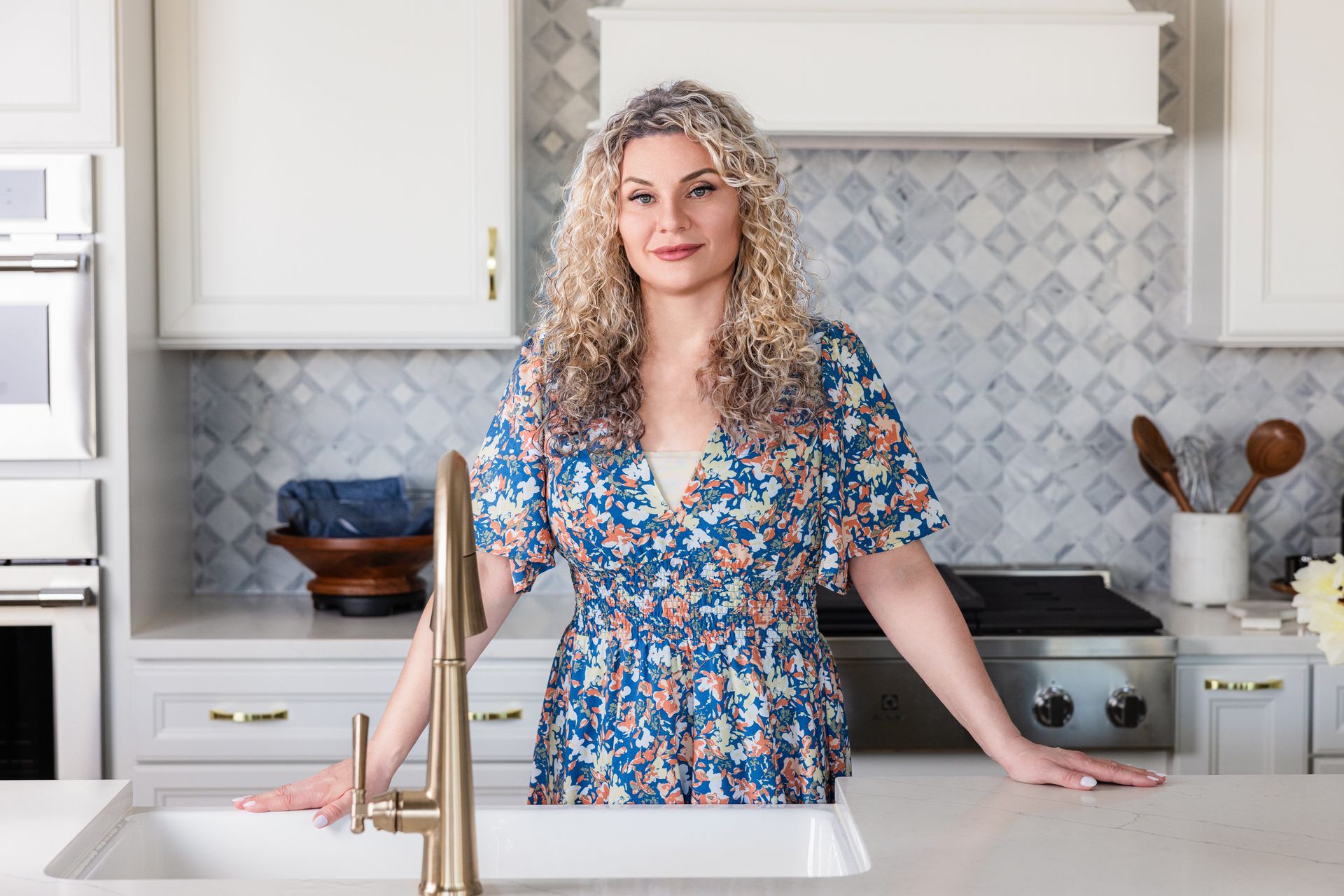 A woman in a blue dress is standing in a kitchen next to a sink.