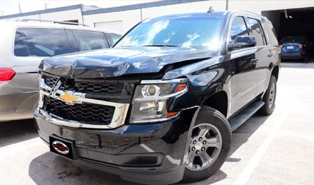 Black Chevrolet Tahoe with front-end damage parked outside.