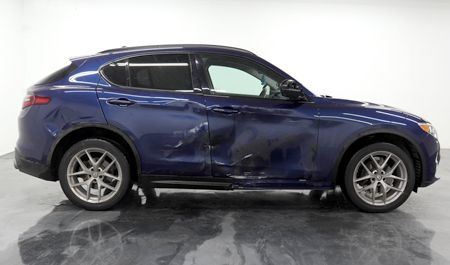 Blue Alfa Romeo SUV with significant damage to the driver's side, parked indoors.