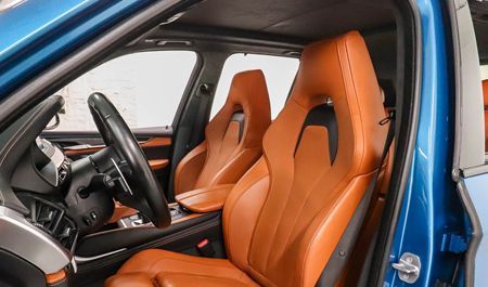 Tan leather interior of a blue BMW with a black steering wheel and a bright, well-lit cabin.