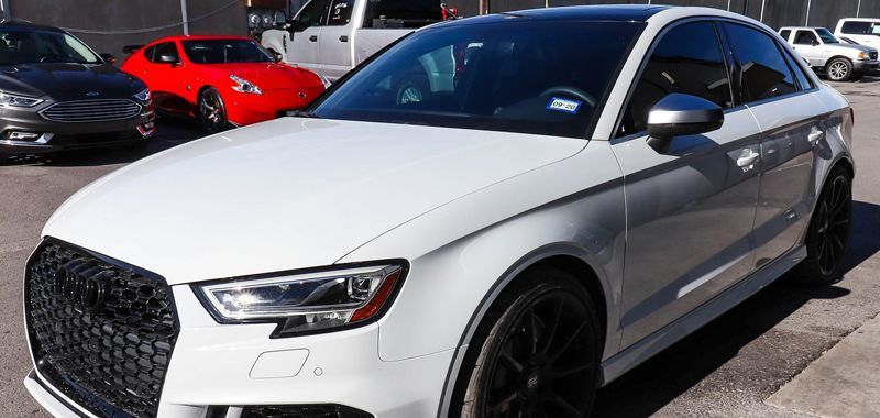 White Audi A3 with black accents parked on asphalt. Other cars are visible in the background.