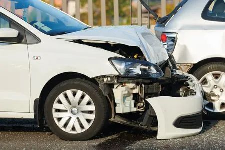 A white car with a crushed hood and damaged front bumper parked behind a silver car after a traffic accident.