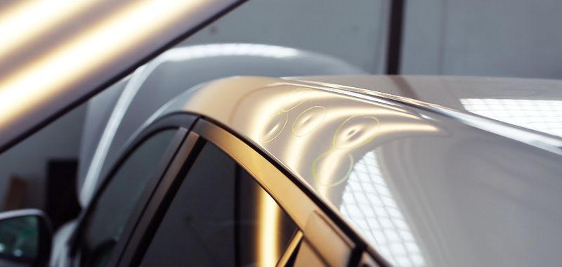 Close-up of a white car roof with several small dents, being inspected in a repair shop.