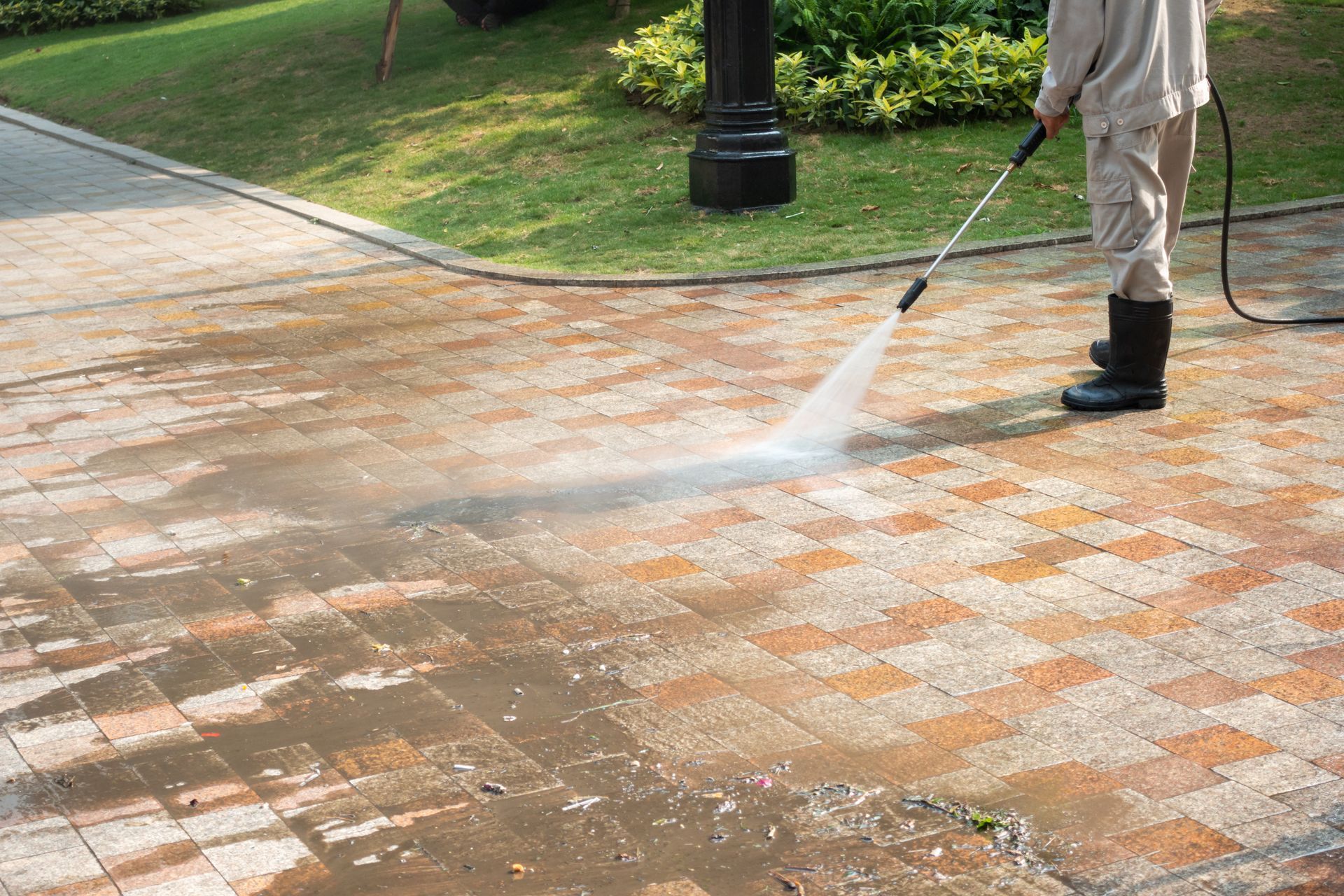 A man is using a high pressure washer to clean a brick driveway.
