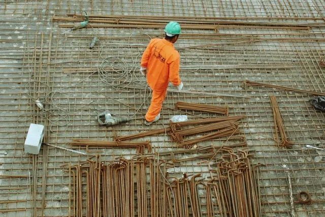 A construction worker is walking on a metal grid at a construction site.