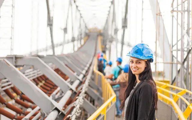 A woman wearing a blue hard hat is standing on a bridge.