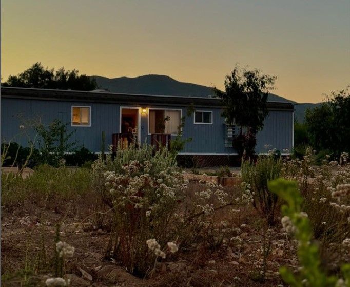 Una casa móvil azul está situada en medio de un campo con montañas al fondo.