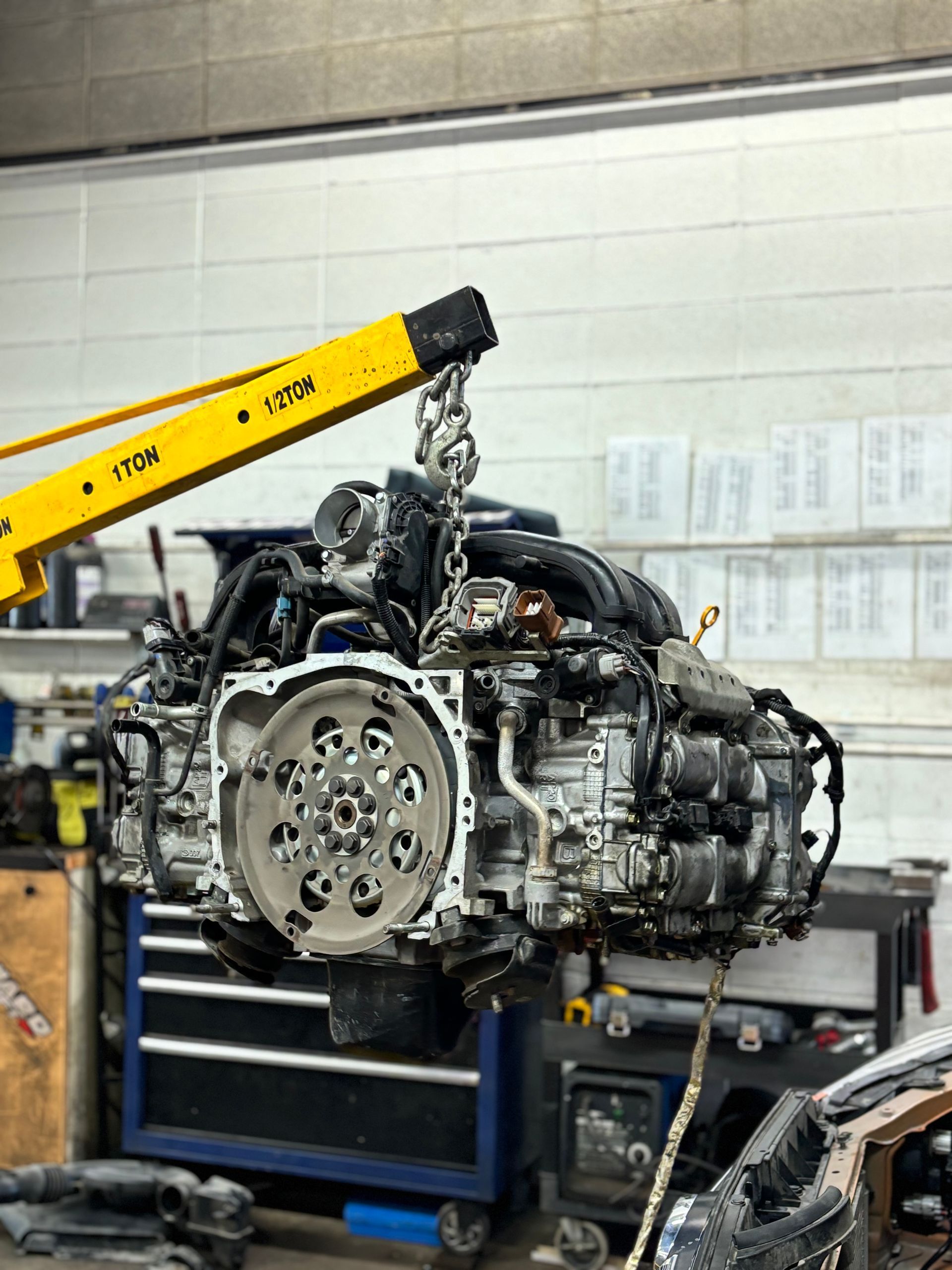 A car engine, suspended by a yellow crane | Economy Auto Repair