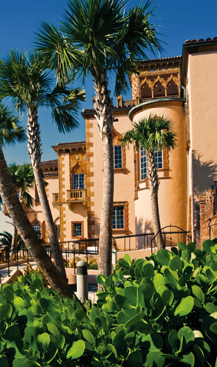 Palm trees frame a beige building with ornate trim, blue sky in the background.