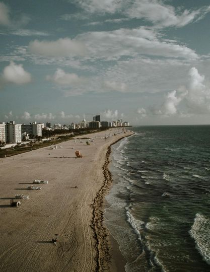 Beach with buildings along the coast under a cloudy sky; waves crash on the shore.
