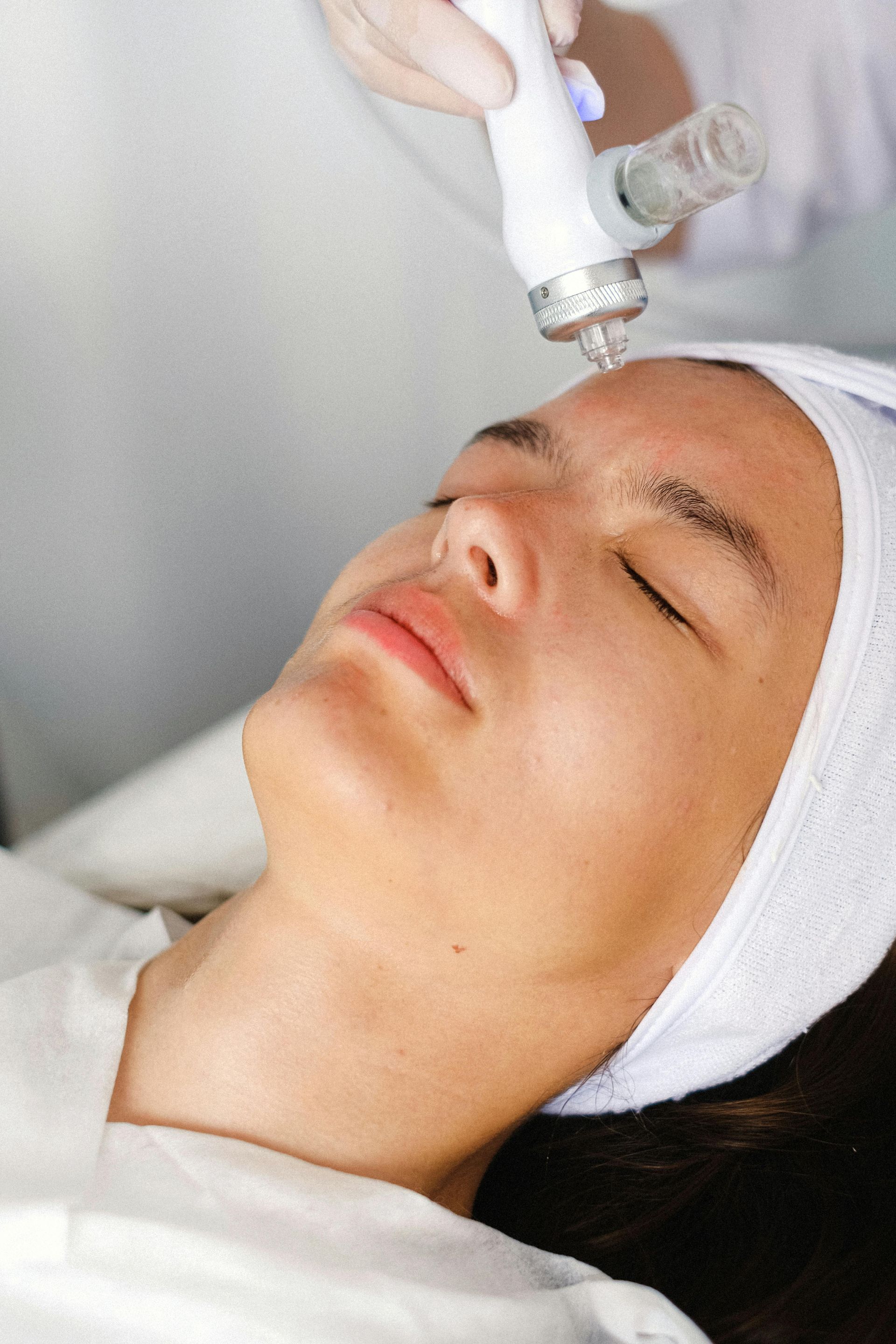 Person receiving facial treatment; technician using a handheld device on the face.