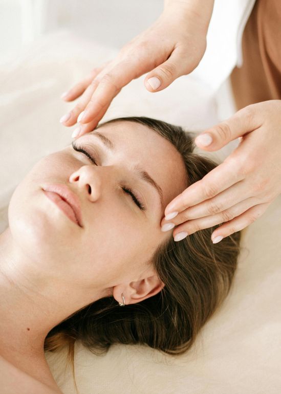 Woman receiving a facial massage, eyes closed, hands above her forehead.