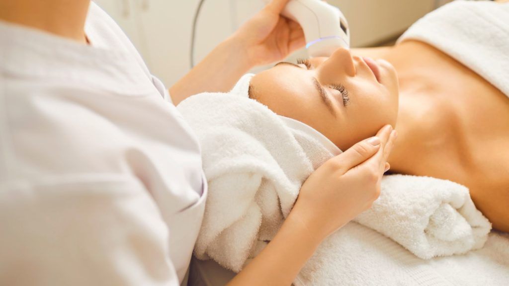 Woman receiving facial treatment at a spa. A beautician uses a device on her face.