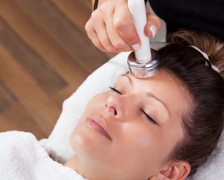 Woman receiving facial treatment with device on forehead.