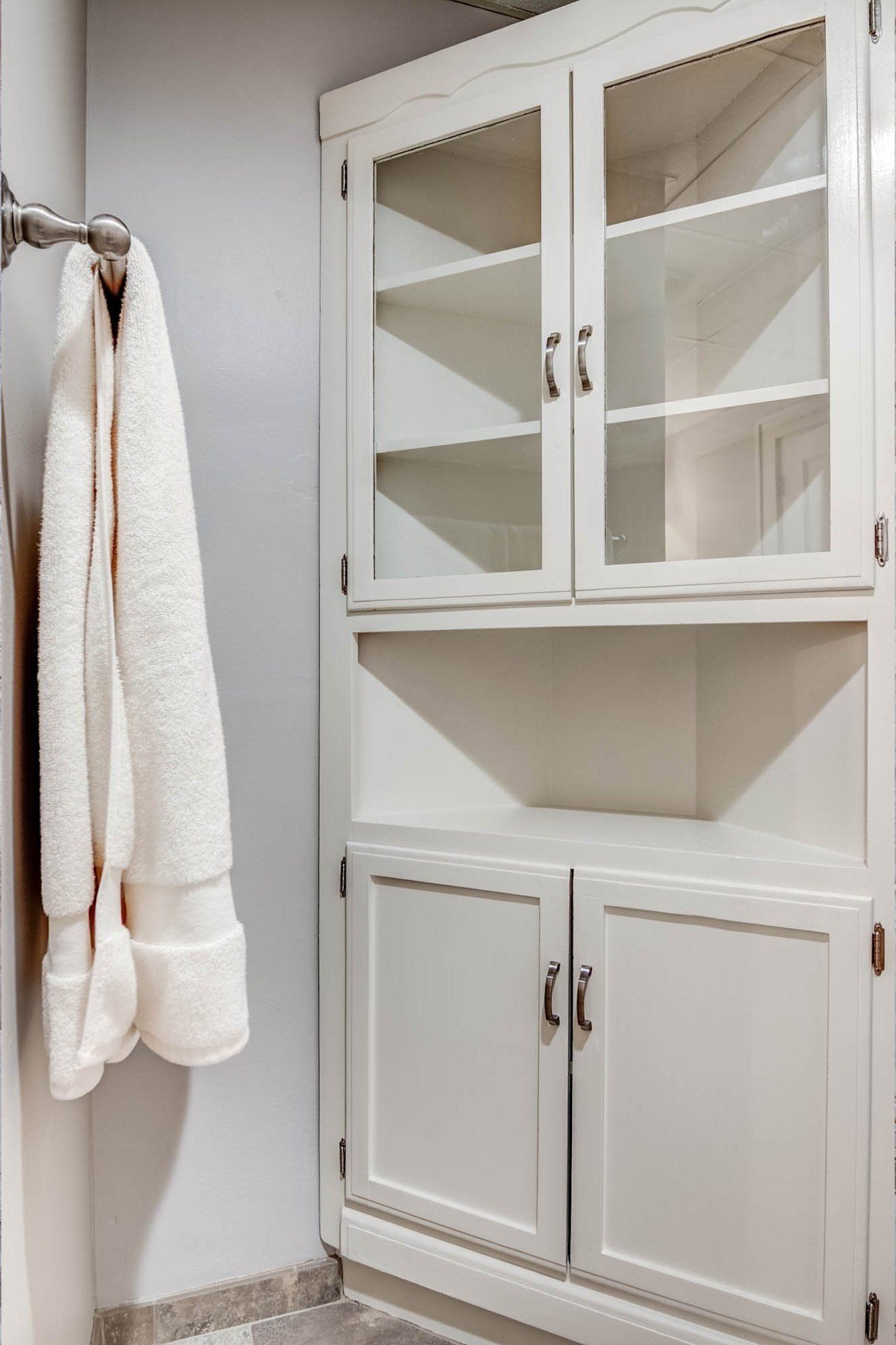 A white cabinet with glass doors and a towel hanging on the wall