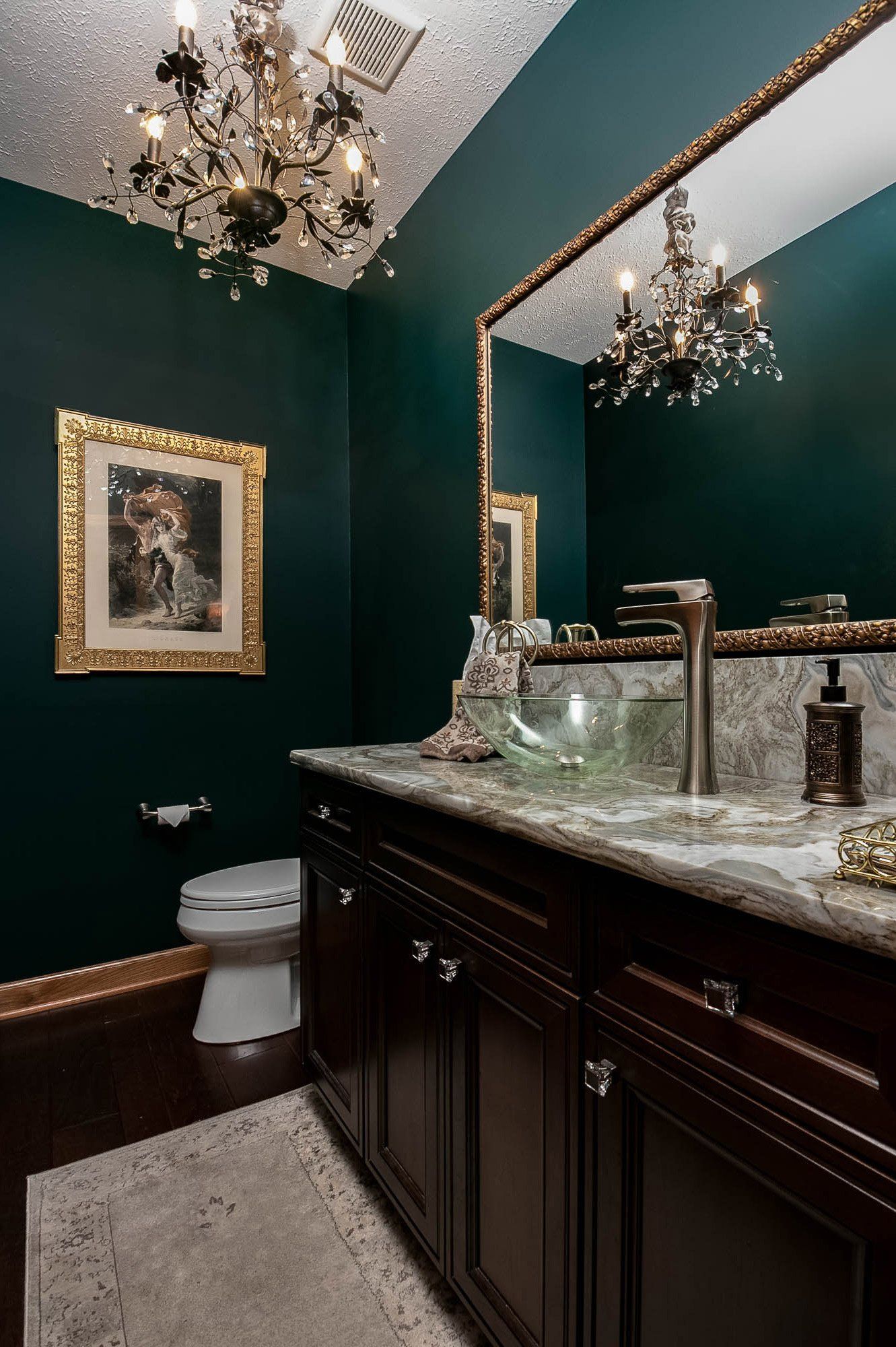 A bathroom with a toilet , sink , mirror and chandelier.