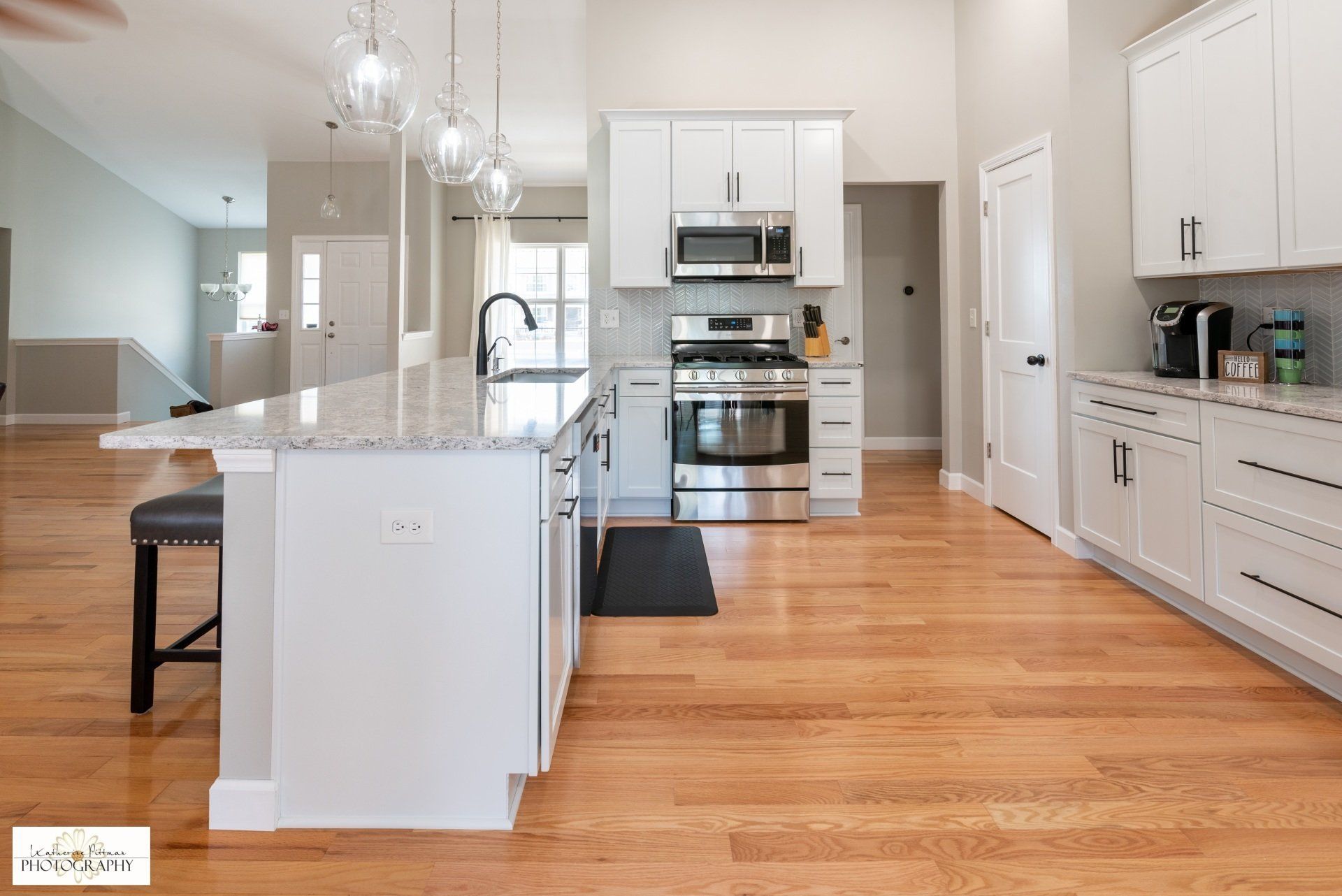 A kitchen with white cabinets , stainless steel appliances , granite counter tops and hardwood floors.