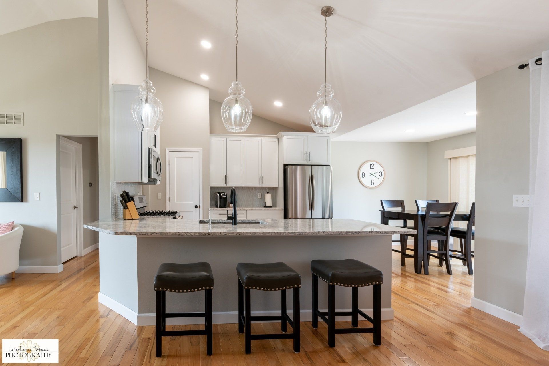 A kitchen with stools and a dining room in the background.