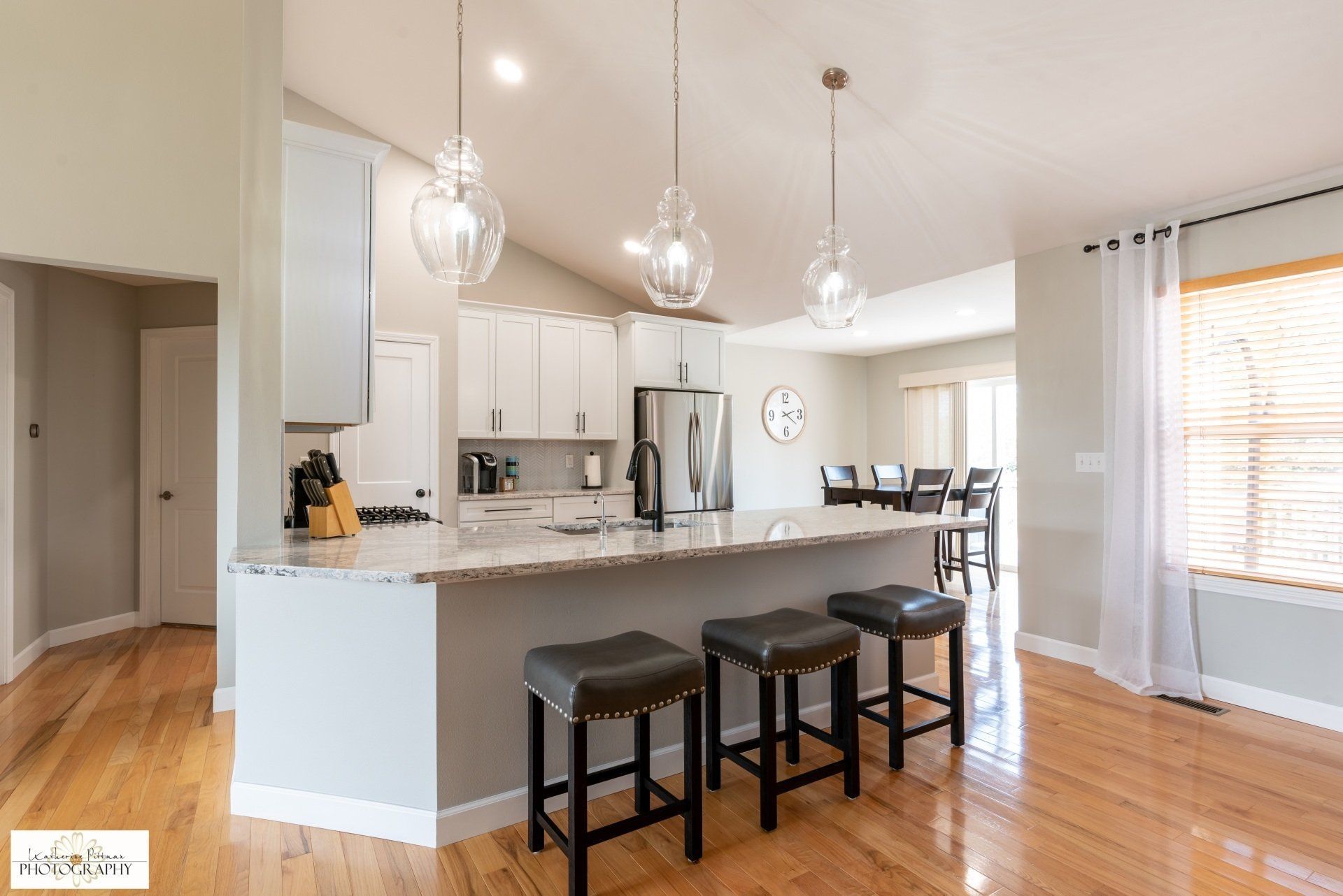 A kitchen with a large island , stools and a refrigerator.