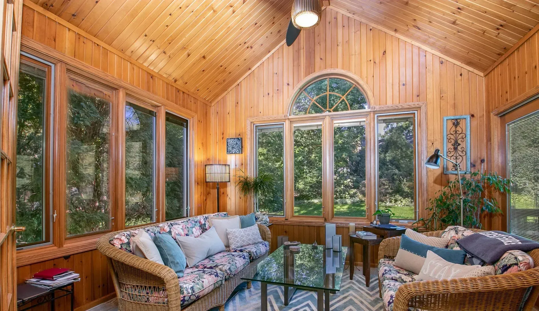 A living room with a couch , chairs , a table and a lot of windows.