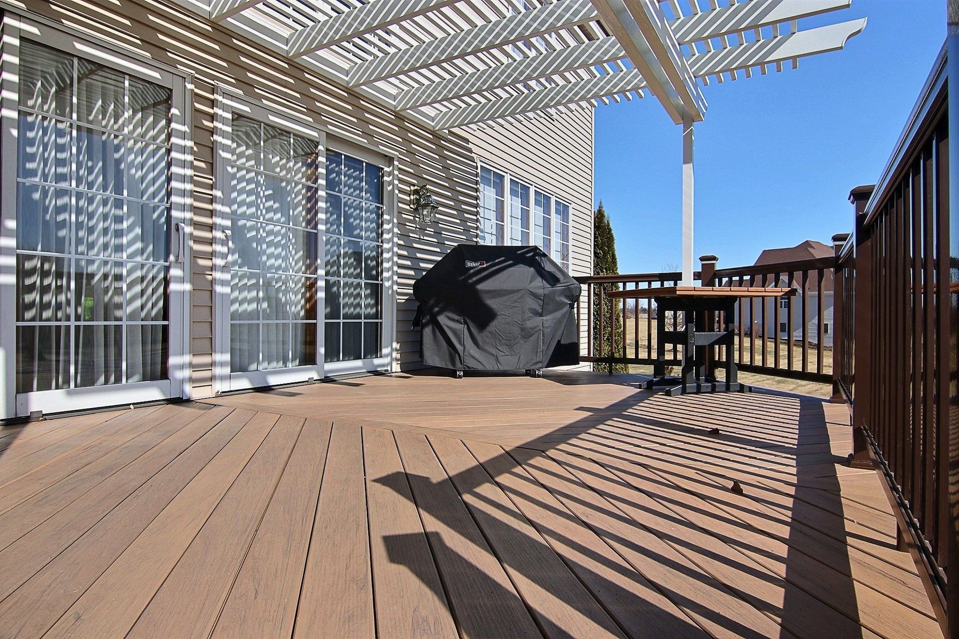 A deck with a grill and a table under a pergola