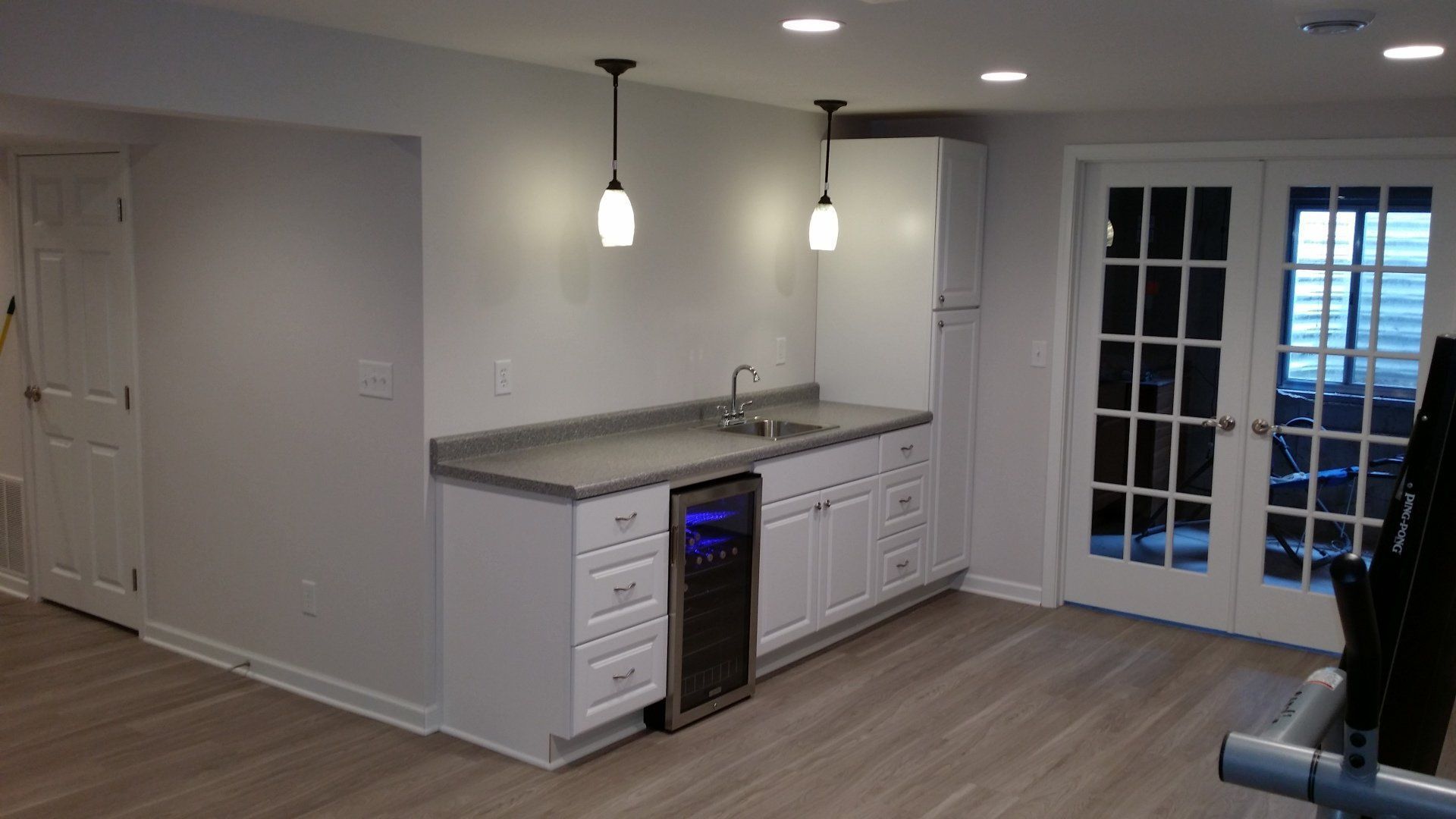 A kitchen with white cabinets , a sink , a refrigerator and french doors.