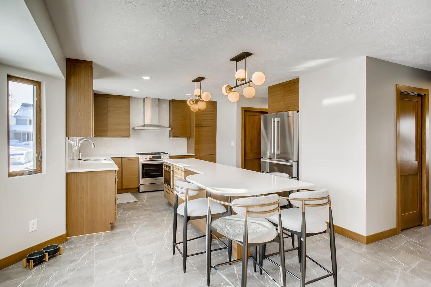 A kitchen with stainless steel appliances , wooden cabinets , a large island with a table and chairs.