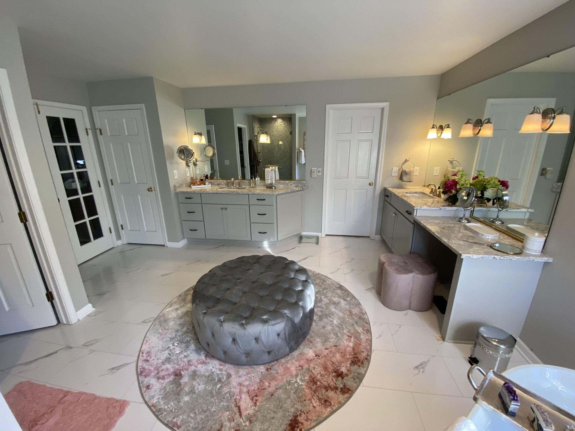 A bathroom with two sinks , a round ottoman , and a large mirror.