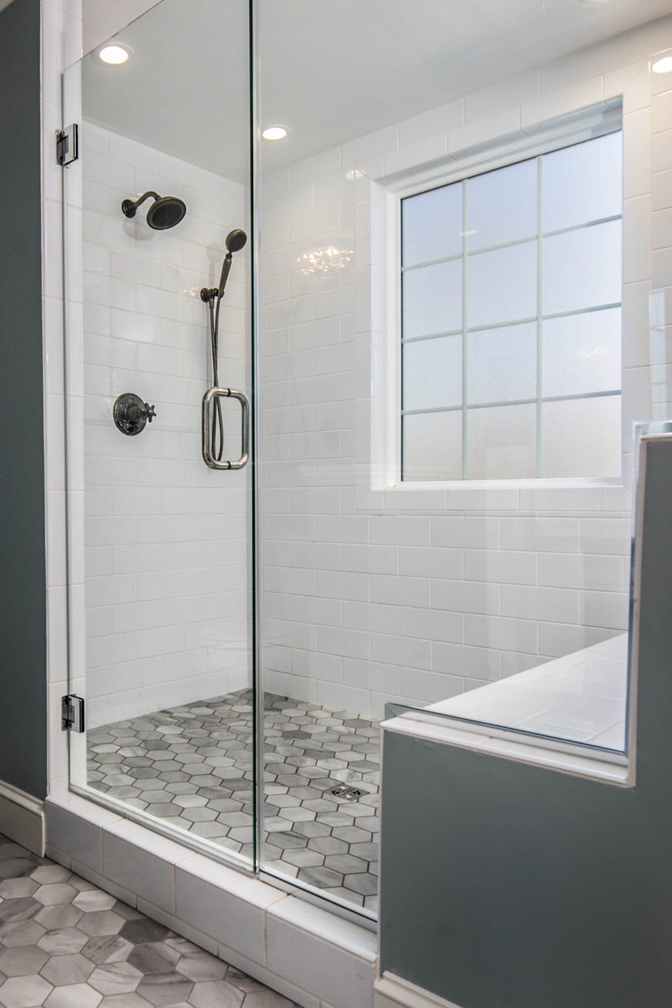 A bathroom with a walk in shower with a glass door and a window.