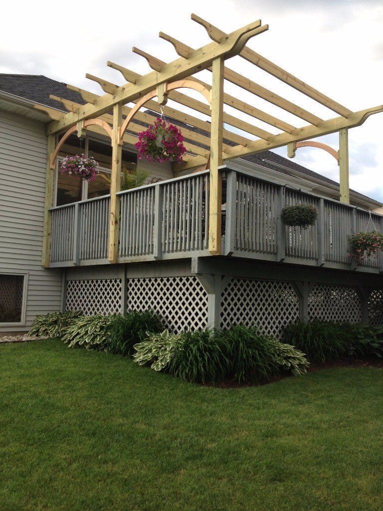 A wooden pergola is sitting on top of a deck next to a house.