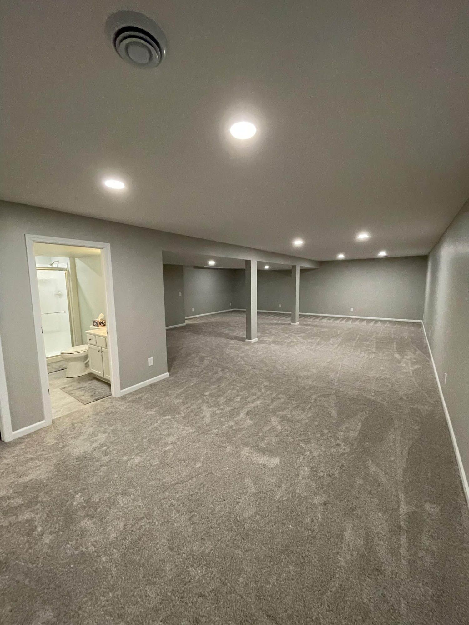 A large empty basement with a carpeted floor and a bathroom.