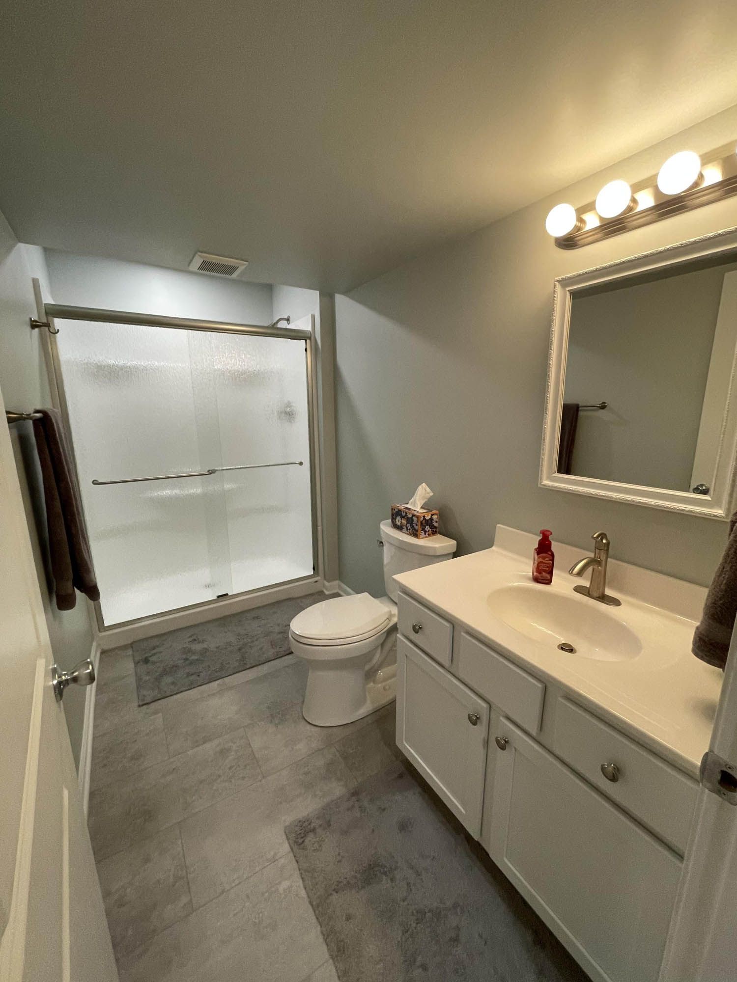 A bathroom with a toilet , sink , mirror and shower.