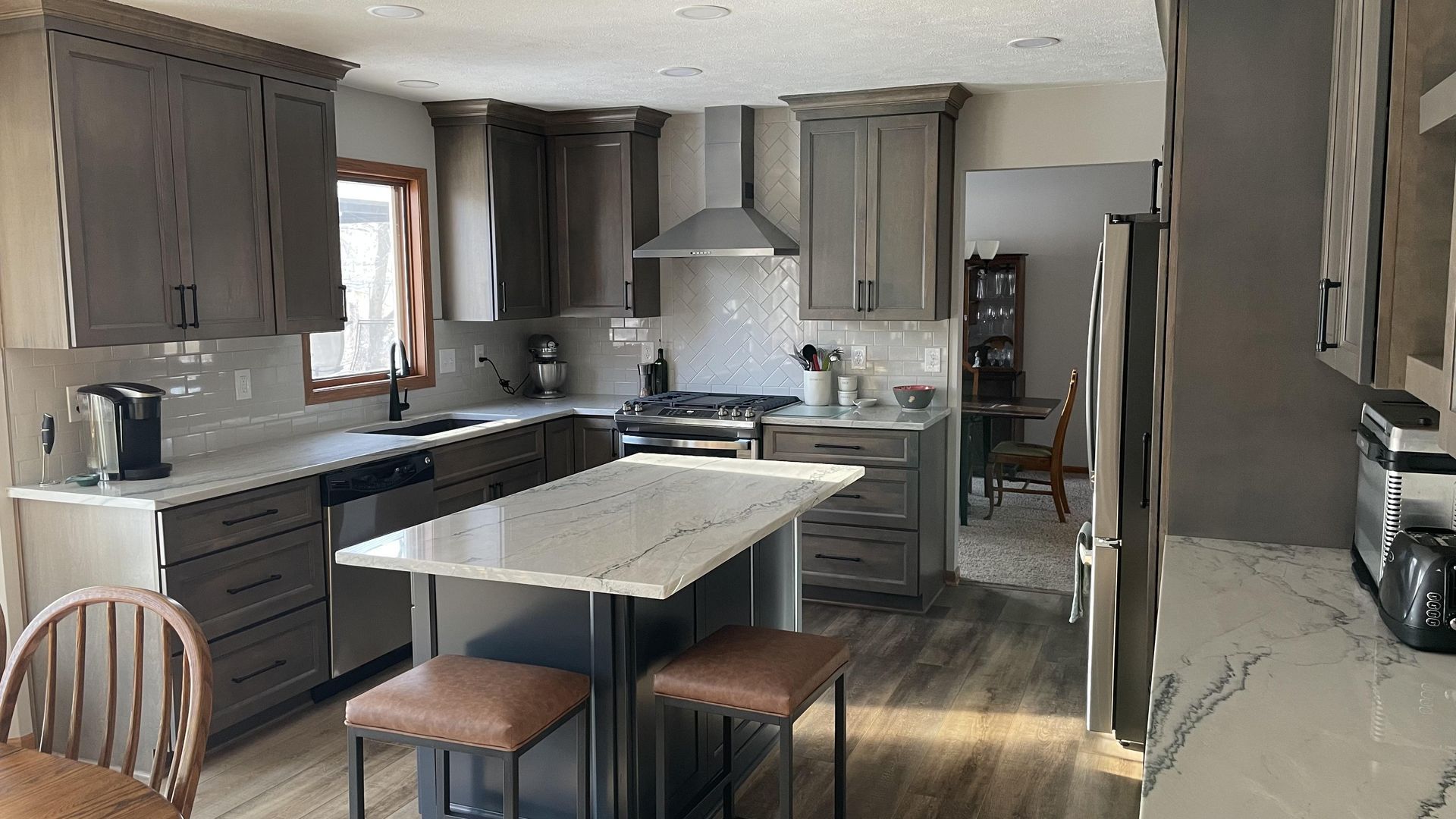 A kitchen with gray cabinets , white counter tops , stainless steel appliances and a large island.