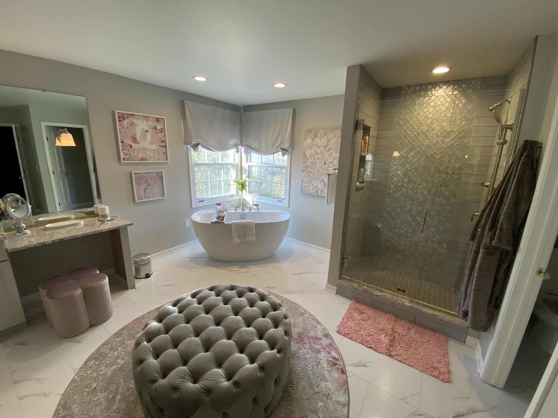 A bathroom with a tub , ottoman , mirror and shower.