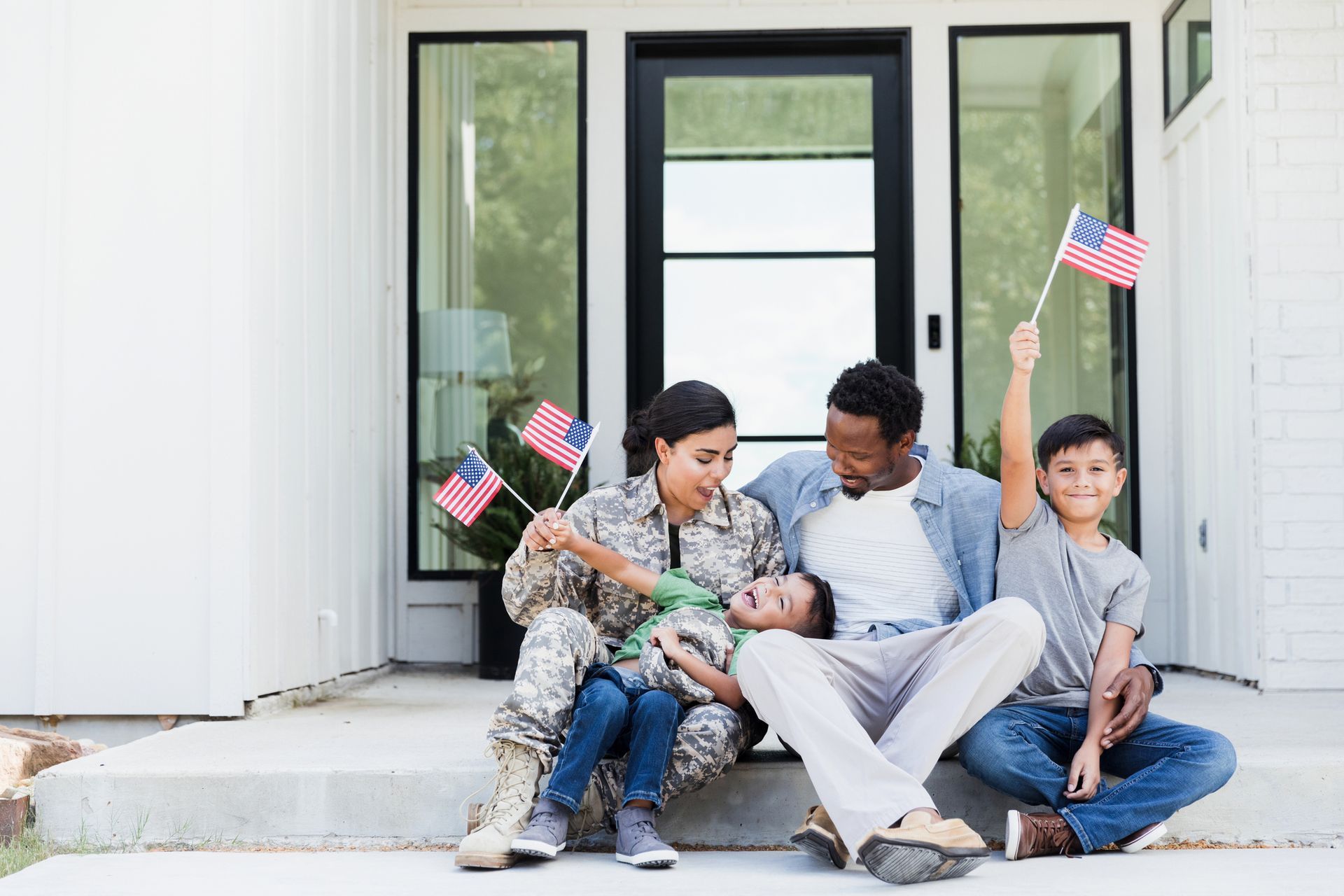 Family, including a woman in uniform, sitting on porch with American flags.