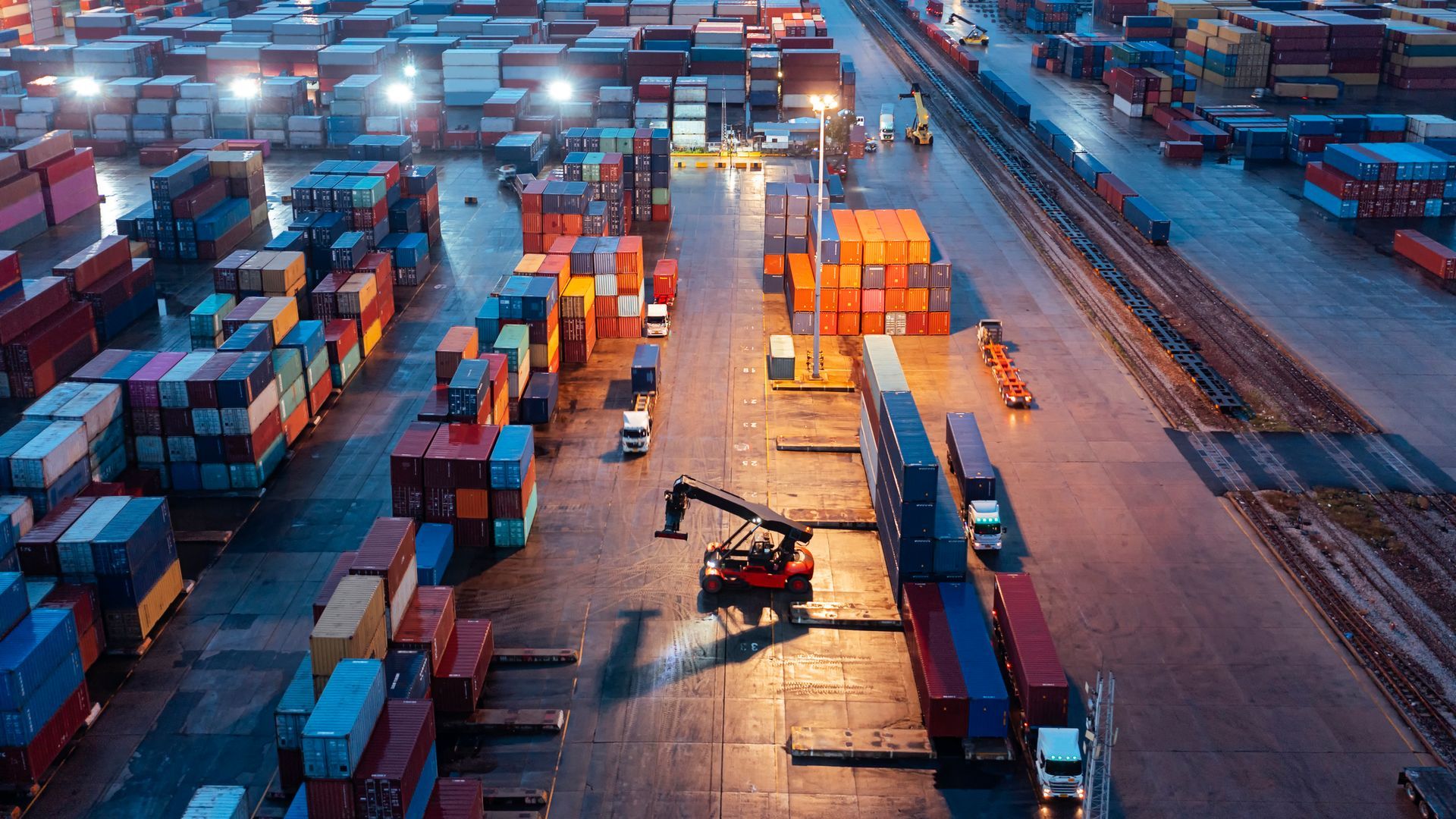 Cargo containers stacked in a port at night with machinery loading.
